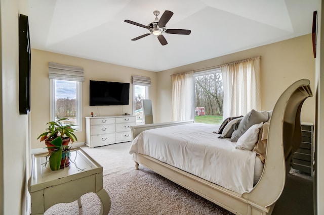 bedroom featuring a tray ceiling, light colored carpet, and ceiling fan