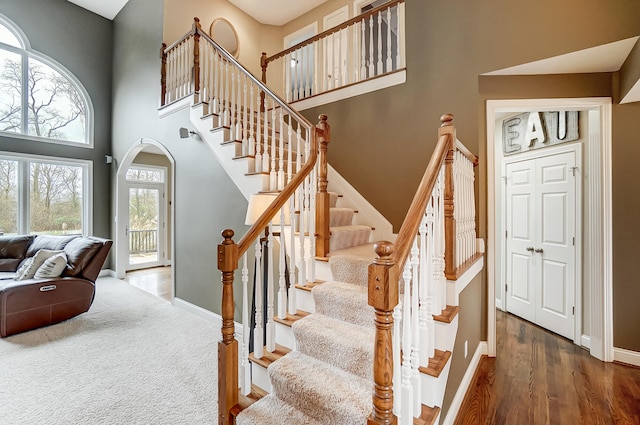 stairs with a towering ceiling, a healthy amount of sunlight, and hardwood / wood-style flooring