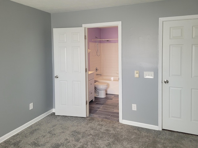 unfurnished bedroom featuring ensuite bath and dark colored carpet