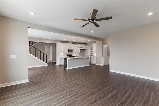 unfurnished living room with dark wood-type flooring, recessed lighting, baseboards, and stairs