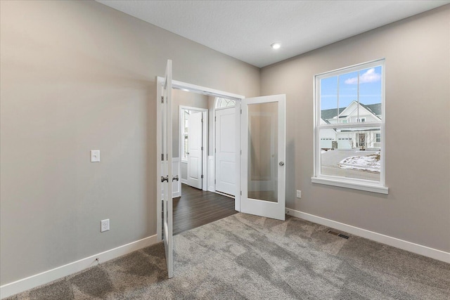 interior space with dark colored carpet, french doors, visible vents, and baseboards