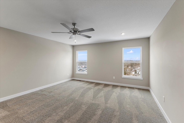 carpeted spare room featuring a ceiling fan, a wealth of natural light, a textured ceiling, and baseboards