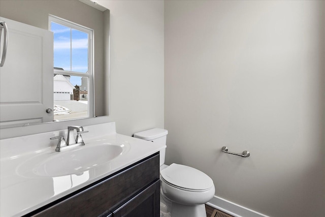 half bathroom featuring toilet, visible vents, baseboards, and vanity