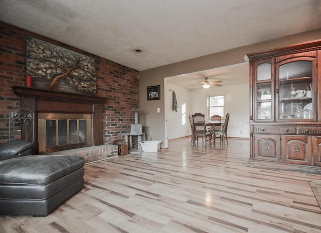 living room with a wood stove, ceiling fan, light hardwood / wood-style floors, a brick fireplace, and a textured ceiling