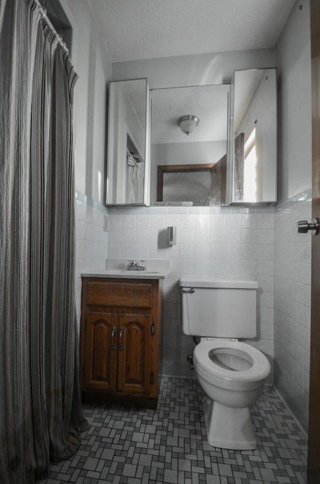 bathroom featuring vanity, tile walls, a textured ceiling, and toilet