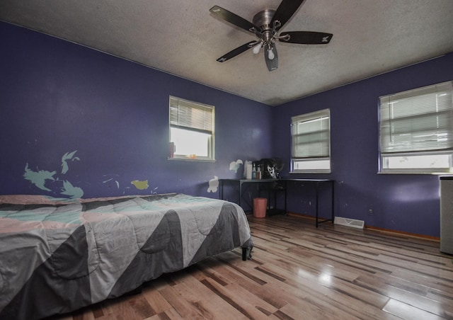 bedroom featuring ceiling fan, hardwood / wood-style floors, and a textured ceiling