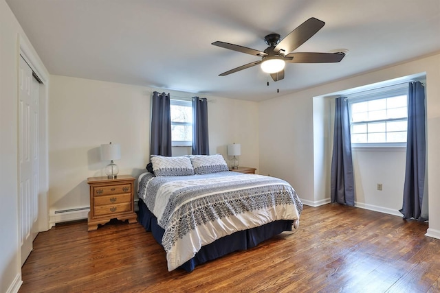 bedroom with a baseboard heating unit, dark wood-type flooring, a closet, and ceiling fan