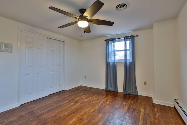 unfurnished bedroom with ceiling fan, dark hardwood / wood-style floors, a closet, and a baseboard heating unit