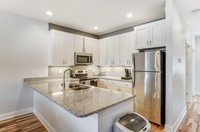 kitchen with sink, appliances with stainless steel finishes, light hardwood / wood-style floors, white cabinets, and kitchen peninsula