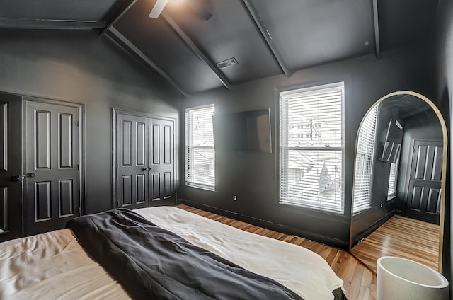 bedroom with hardwood / wood-style flooring, ceiling fan, two closets, and vaulted ceiling with beams