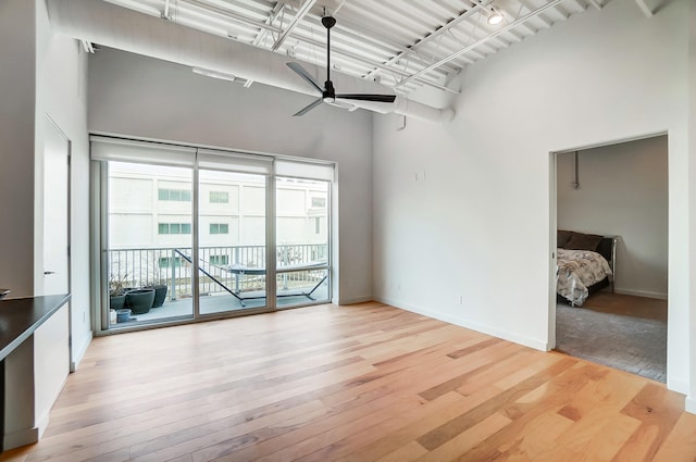 spare room featuring light wood finished floors, a high ceiling, baseboards, and a ceiling fan