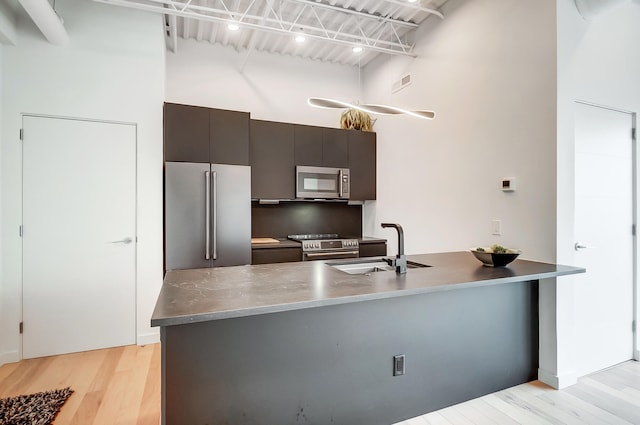 kitchen with light wood-style flooring, stainless steel appliances, a high ceiling, a peninsula, and a sink