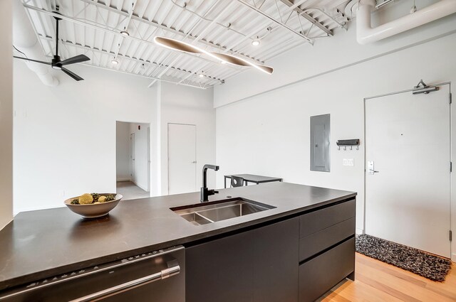 kitchen with light wood finished floors, electric panel, dark countertops, dishwashing machine, and a sink