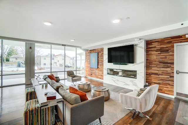 living room with wooden walls, a premium fireplace, wood finished floors, floor to ceiling windows, and recessed lighting