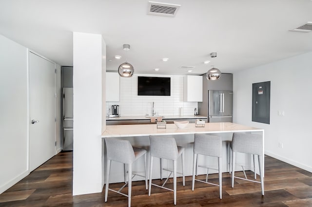 kitchen with visible vents, high end fridge, dark wood-style floors, tasteful backsplash, and a kitchen bar