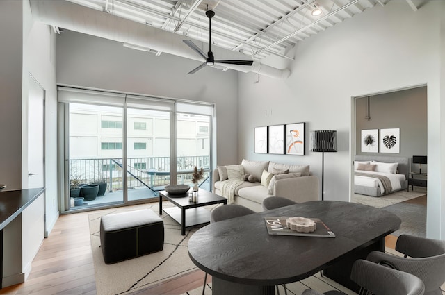 living area featuring light wood-style flooring, a towering ceiling, and a ceiling fan