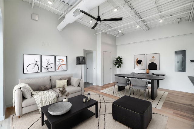 living area with light wood finished floors, electric panel, visible vents, a ceiling fan, and a towering ceiling