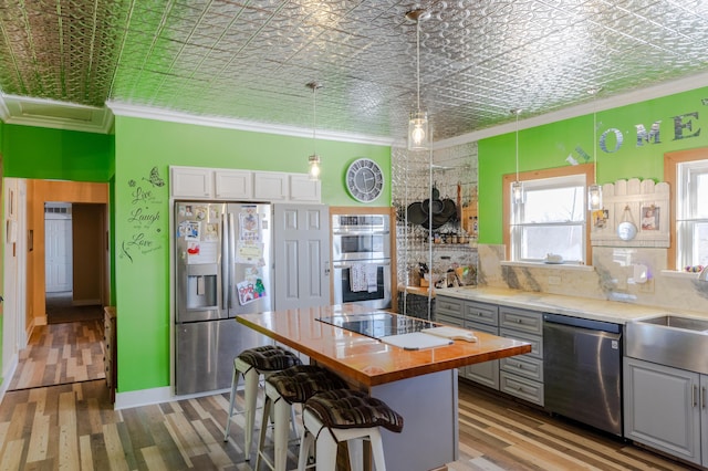 kitchen with appliances with stainless steel finishes, decorative light fixtures, white cabinetry, wooden counters, and ornamental molding