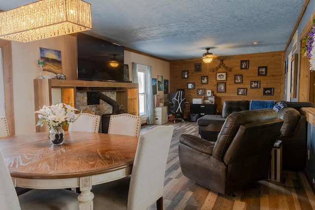 dining room with ceiling fan, hardwood / wood-style flooring, a textured ceiling, and wood walls