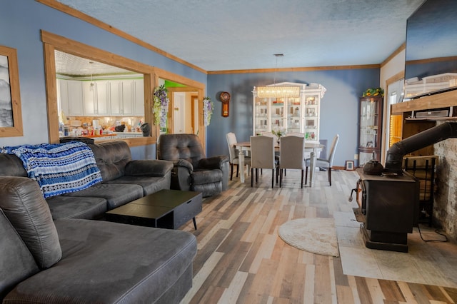 living room featuring ornamental molding, a textured ceiling, light wood-type flooring, a chandelier, and a wood stove