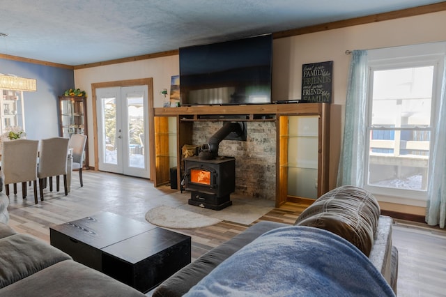 living room featuring ornamental molding, light hardwood / wood-style floors, a textured ceiling, french doors, and a wood stove