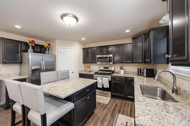 kitchen featuring appliances with stainless steel finishes, dark hardwood / wood-style floors, sink, a kitchen bar, and light stone counters