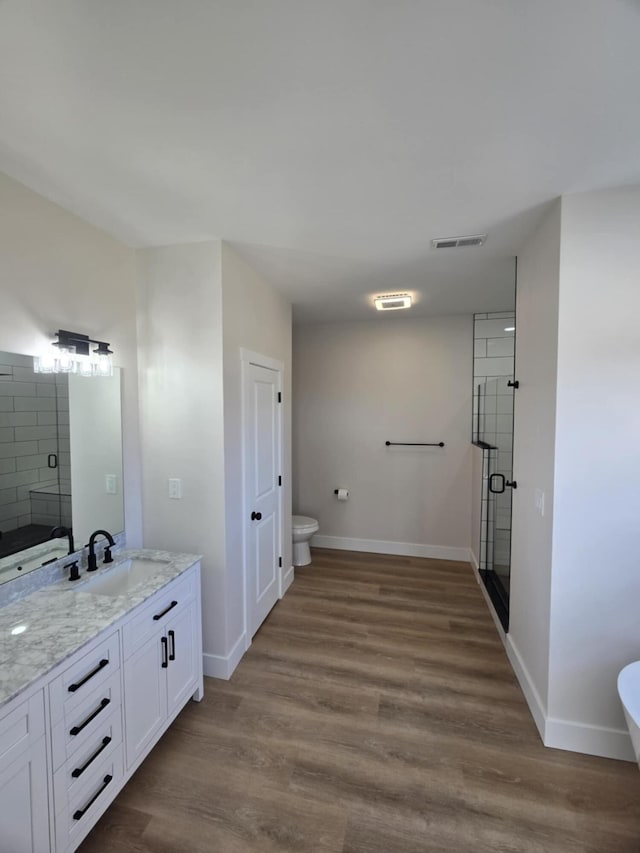 bathroom featuring vanity, hardwood / wood-style flooring, a shower with shower door, and toilet