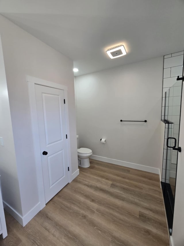 bathroom with wood-type flooring, toilet, and a shower with door