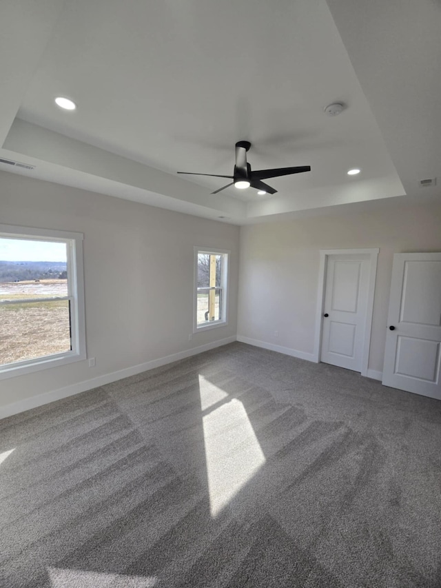 carpeted empty room with a raised ceiling and ceiling fan