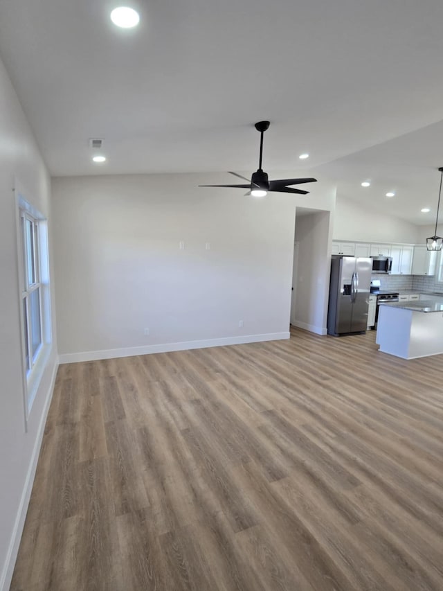 unfurnished living room with ceiling fan, vaulted ceiling, and light wood-type flooring