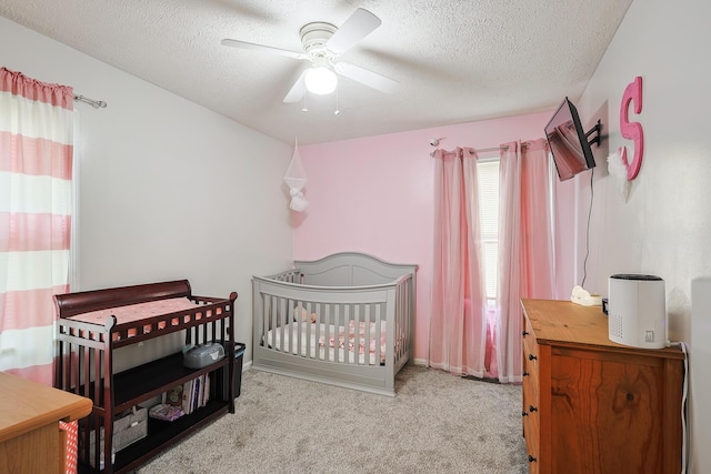 bedroom with a nursery area, ceiling fan, light carpet, and a textured ceiling