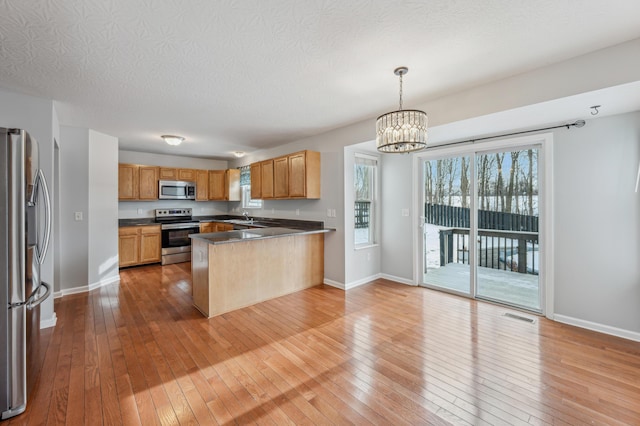 kitchen with decorative light fixtures, light hardwood / wood-style floors, kitchen peninsula, and appliances with stainless steel finishes