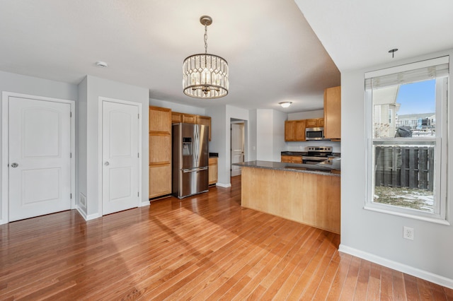 kitchen with appliances with stainless steel finishes, pendant lighting, a chandelier, light hardwood / wood-style floors, and kitchen peninsula