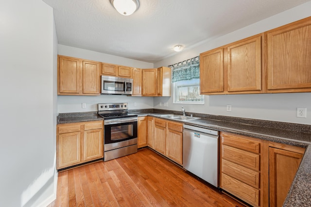 kitchen with appliances with stainless steel finishes, sink, and light hardwood / wood-style flooring