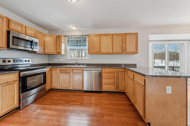 kitchen with sink, wood-type flooring, kitchen peninsula, and appliances with stainless steel finishes