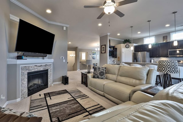 living room featuring crown molding, light colored carpet, a stone fireplace, and ceiling fan with notable chandelier