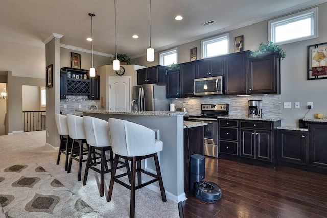 kitchen with pendant lighting, a breakfast bar, a kitchen island with sink, stainless steel appliances, and light stone counters