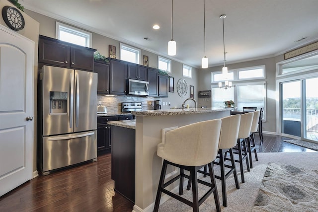 kitchen with a breakfast bar, appliances with stainless steel finishes, ornamental molding, a center island with sink, and decorative light fixtures