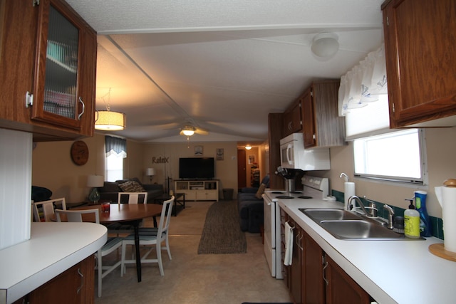 kitchen featuring lofted ceiling, light countertops, a sink, white appliances, and plenty of natural light