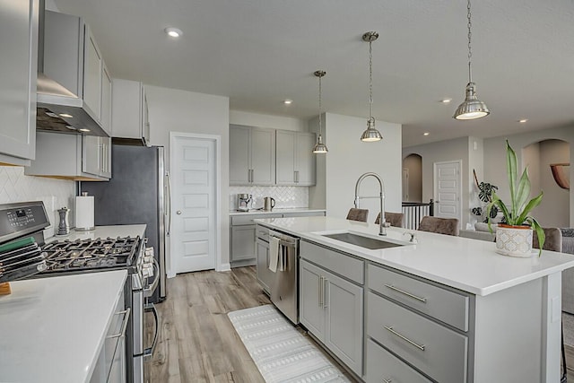 kitchen with arched walkways, a center island with sink, light countertops, appliances with stainless steel finishes, and a sink