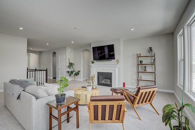 living area with arched walkways, recessed lighting, light carpet, baseboards, and a glass covered fireplace