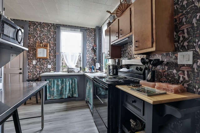 kitchen featuring black / electric stove, dark brown cabinetry, exhaust hood, and light wood-type flooring