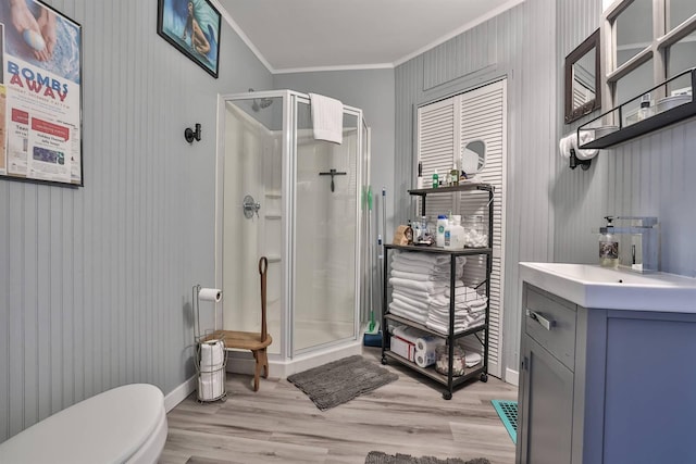 bathroom with crown molding, a shower with door, hardwood / wood-style floors, vanity, and toilet