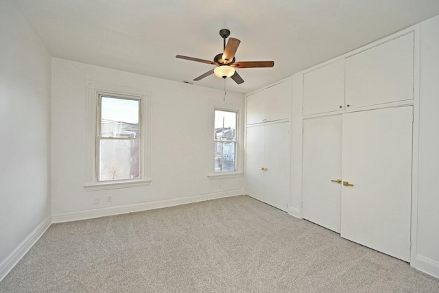 unfurnished bedroom featuring multiple closets, light carpet, and ceiling fan