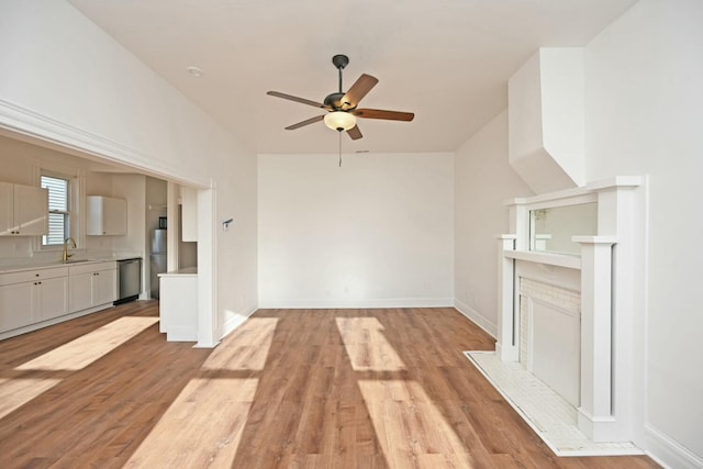 unfurnished living room with ceiling fan, sink, a fireplace, and light hardwood / wood-style floors