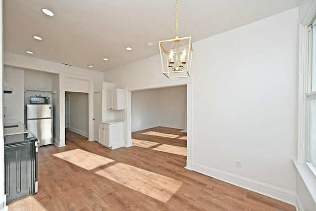 kitchen featuring white cabinetry, hanging light fixtures, light hardwood / wood-style floors, and stainless steel refrigerator