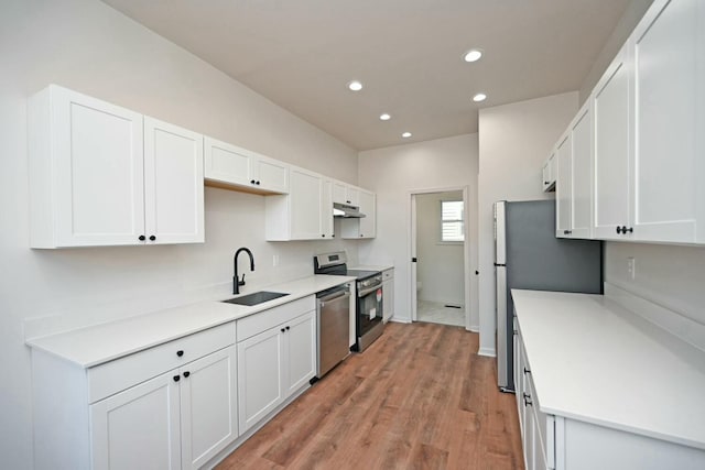 kitchen with appliances with stainless steel finishes, sink, white cabinets, and light hardwood / wood-style flooring