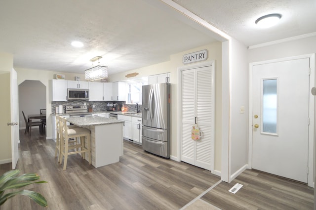 kitchen featuring appliances with stainless steel finishes, a breakfast bar, white cabinetry, a center island, and light stone counters