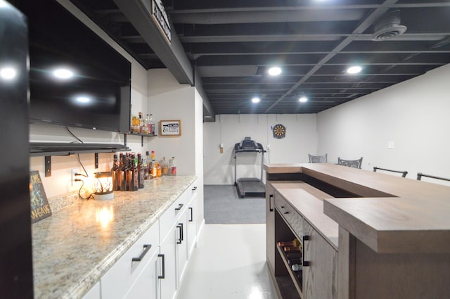 bar with light stone countertops, concrete floors, and white cabinets