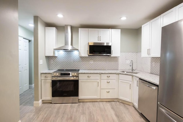 kitchen featuring sink, white cabinets, light stone counters, stainless steel appliances, and wall chimney exhaust hood